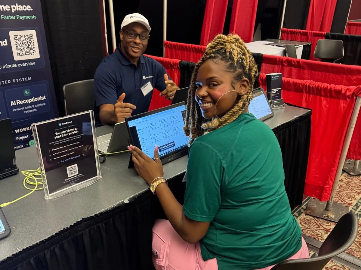A conference attendee trying ServGround on a laptop at the booth while David Obim points to the screen