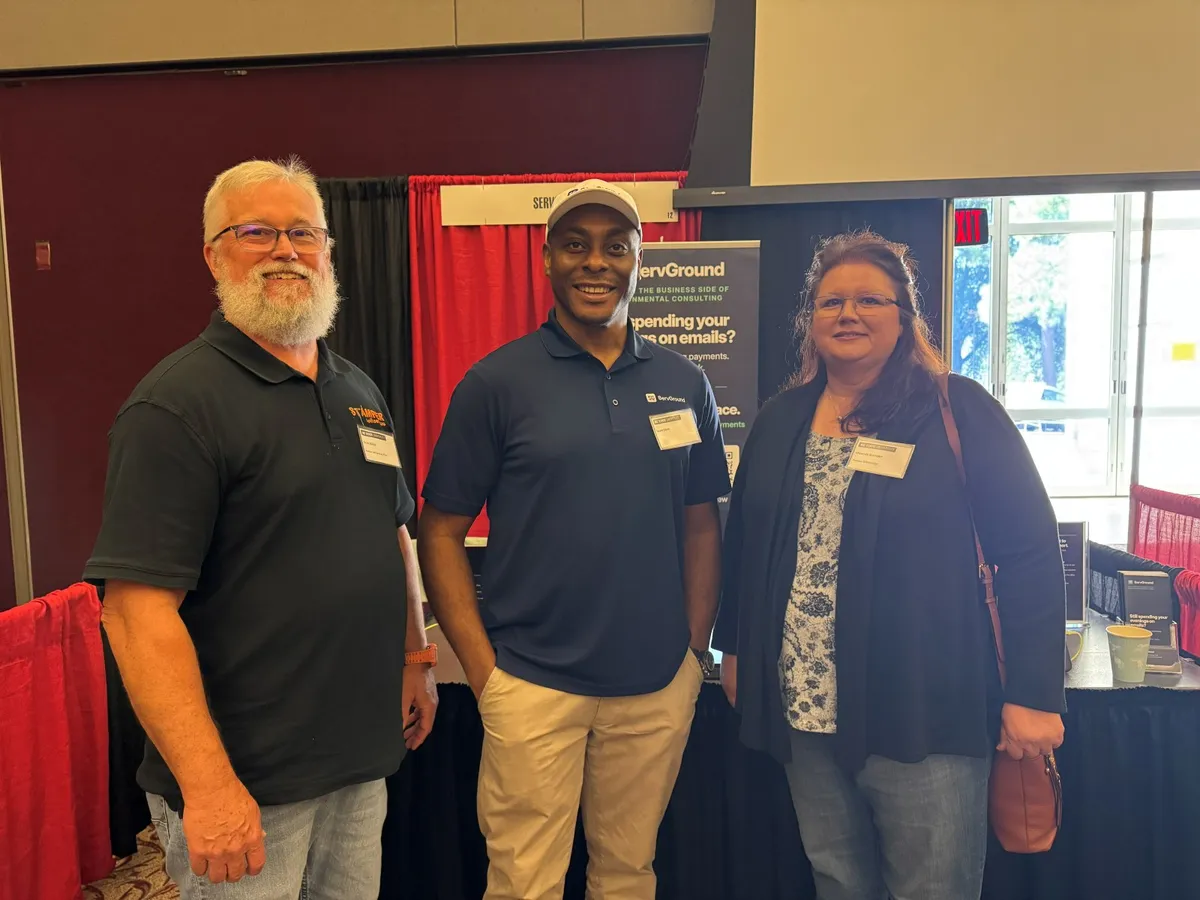 David Obim with two conference attendees in front of the ServGround booth