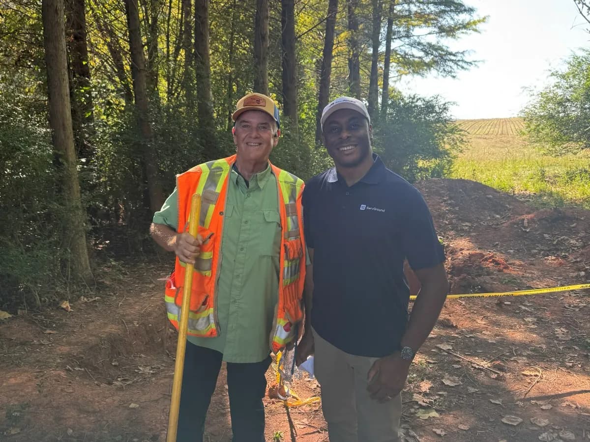 David Obim with a field professional holding a shovel beside an open soil pit in the woods