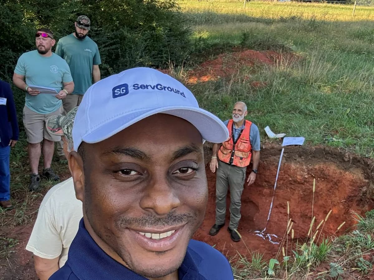David Obim at a soil pit field day, with professionals gathered around an open pit with a measuring tape